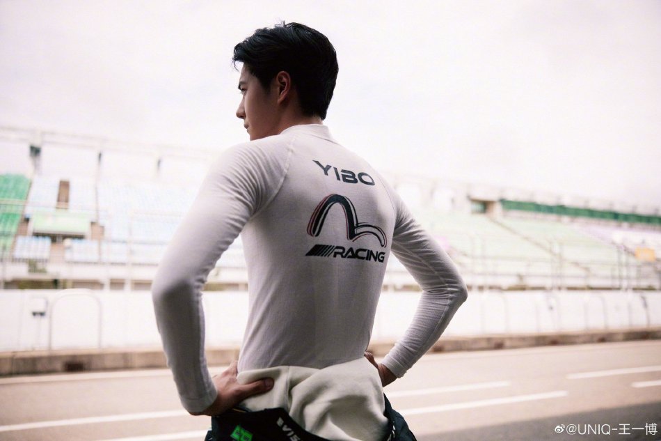 王一博微博分享赛车场随拍照 黑绿赛车服单手拿头盔帅气十足